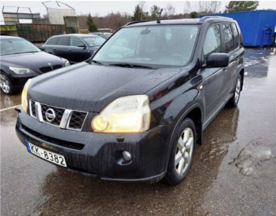 Melna Nissan markas automašīna ar ieslēgtiem priekšējiem lukturiem